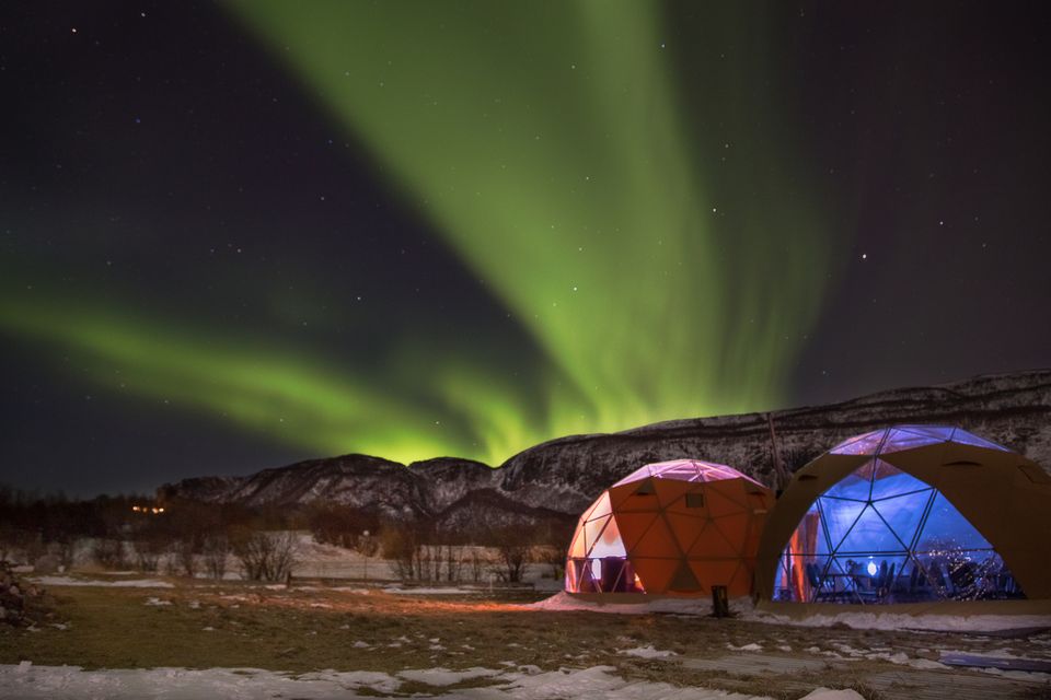 Outside Bodø, the aurora borealis shines brightly over two clear, plastic tent igloos used for viewing. Photo: Getty